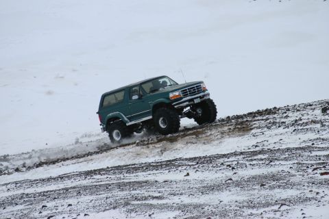 1996 Ford Bronco - A lifted green 1996 Ford Bronco navigates a challenging snowy incline with large tires.