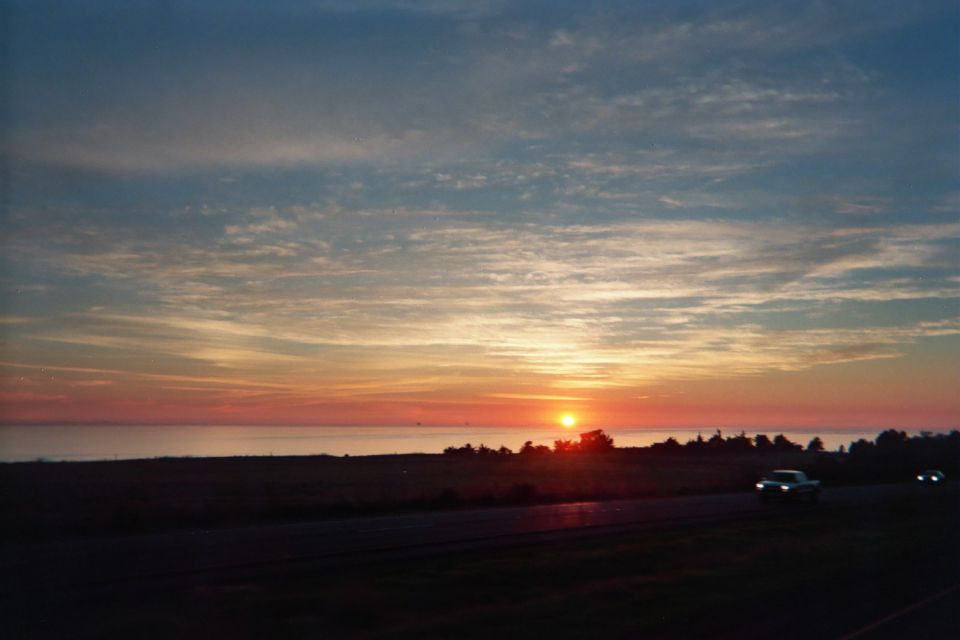 Orange sunset over a flat horizon with streaked clouds and a car on a roadside below