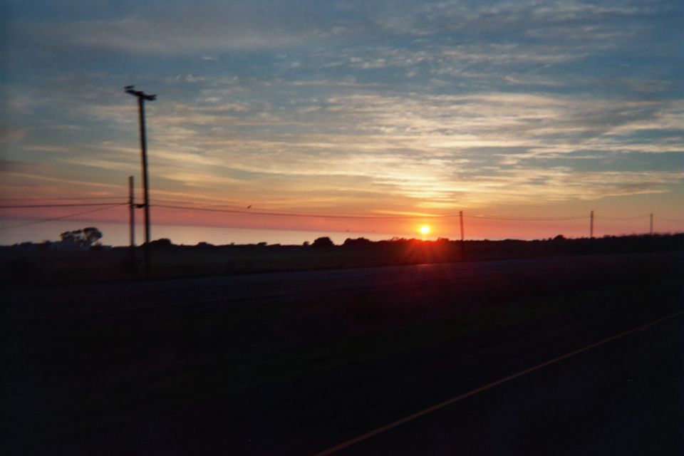 Sunset over flat farmland with a utility pole and power lines silhouetted against the sky