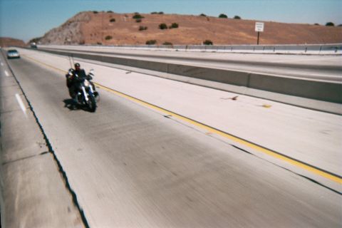 1990 Ford Bronco - lone motorcyclist rides down a wide concrete multi-lane highway past a dry brown hillside under a clear sky.