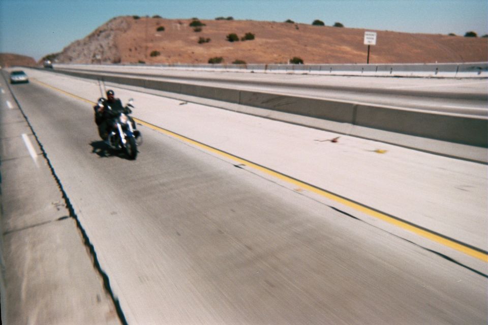 Motorcyclist riding on a wide concrete highway past a dry hillside