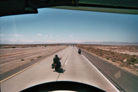 1990 Ford Bronco - Seen from within a vehicle, two loaded motorcycles ride a straight desert highway flanked by scrub and distant mountains.