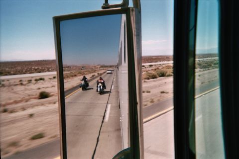 1990 Ford Bronco - View through a vehicle side mirror of two motorcycles riding on a two-lane desert highway under clear sky.