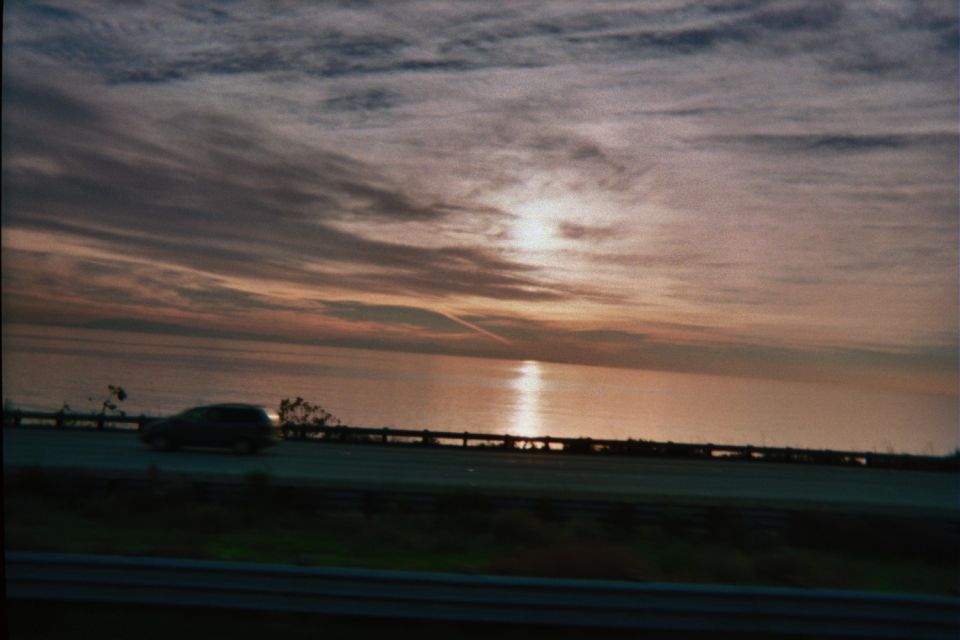 Sunset over water beside a highway with a passing silver car