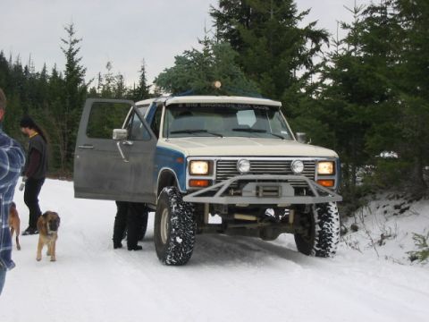 1995 Ford Bronco - A two-tone Ford Bronco with a Christmas tree on its roof is parked in the snow, with people and dogs nearby.