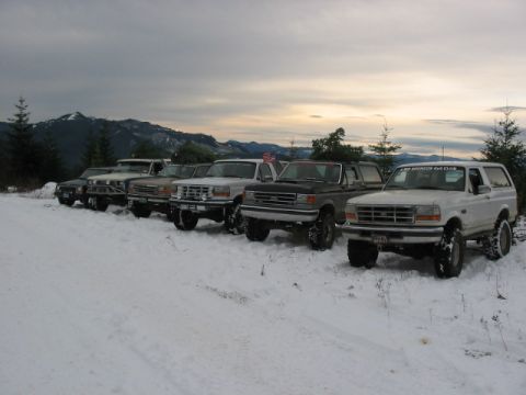 1995 Ford Bronco - A line of Ford Broncos, including a white 1995 model with a club sticker, parked in the snow on a mountain road.