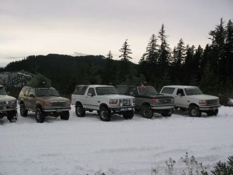 1995 Ford Bronco - Several Ford Broncos and an SUV are parked in a snowy landscape with trees and hills.