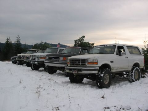 1995 Ford Bronco - A line of Ford Broncos parked in a snowy landscape under an overcast sky.