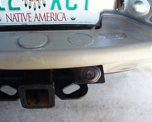 Backup camera mounted above trailer hitch receiver on tan rear bumper with Native America license plate