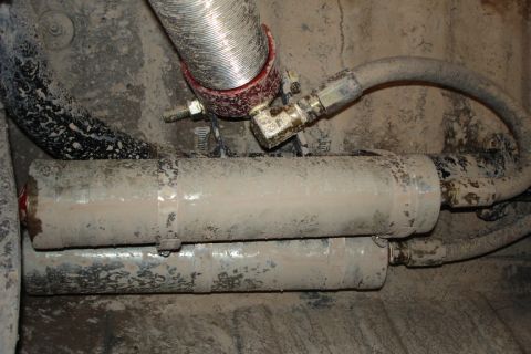 1987 Ford Bronco - Close-up view of dirty exhaust components and hoses under a vehicle.