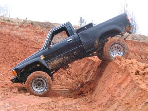 1986 Ford F-150 - This black pickup truck is navigating a challenging off-road course, demonstrating its capabilities on a steep, muddy incline.