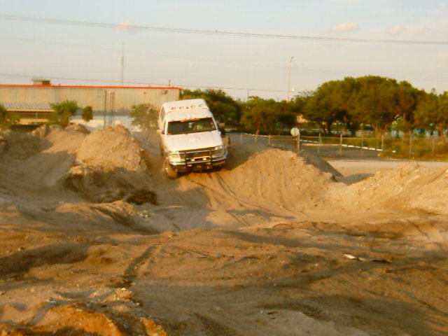 White van driving up a dirt mound. The van has text on its side