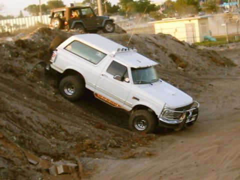 1995 Ford Bronco - A white Ford Bronco navigates a steep dirt incline, with another Jeep visible in the background.