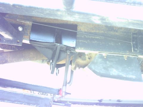 1995 Ford Bronco - Overexposed undercarriage shot looking up at a truck's frame rail and crossmember, with a fabricated black steel bracket, a threaded rod an…