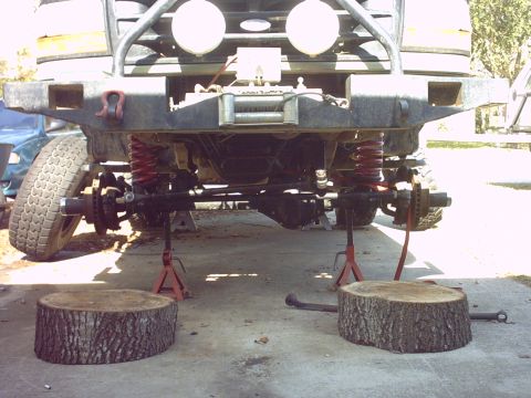 1995 Ford Bronco - Low front view under a lifted Ford 4x4 raised on red jack stands on a concrete driveway, with the front wheels off and the Dana solid front…