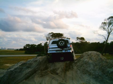 1995 Ford Bronco - A white SUV navigates a dirt mound under a cloudy sky.