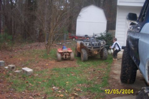 1979 Ford F-150 - A child interacts with a large ATV next to a smaller ATV and a pickup truck in a yard, with a shed in the background.