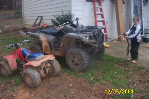 1979 Ford F-150 - Two ATVs are parked in a muddy yard next to a garage, with a child spraying one with a hose.