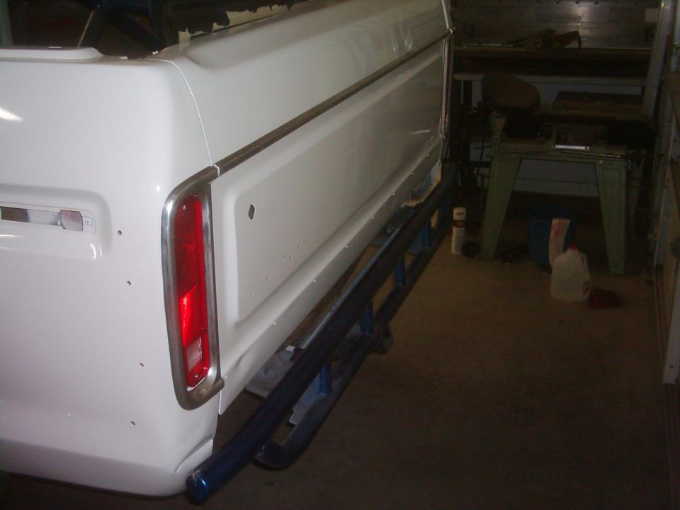White pickup truck tailgate with chrome trim and red taillight, blue step bars installed