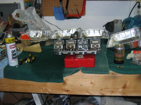 1985 Ford LTD Crown Victoria - A set of four carburetors sits on a workbench next to a can of carb cleaner and various tools, suggesting a repair or maintenance session.