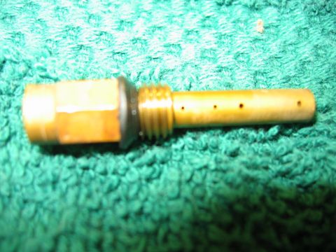 1985 Ford LTD Crown Victoria - A brass carburetor jet, likely from an older vehicle, is shown against a green textured background.