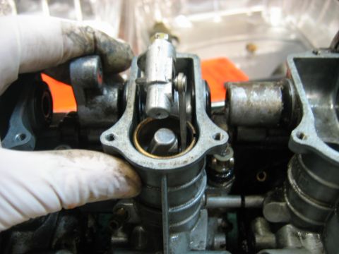 1985 Ford LTD Crown Victoria - A gloved hand manipulates the internal mechanism of a carburetor during maintenance.