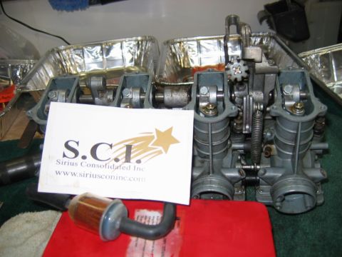 1985 Ford LTD Crown Victoria - A close-up view of a carburetor assembly, with a business card from Sirius Consolidated Inc. placed in front of it.