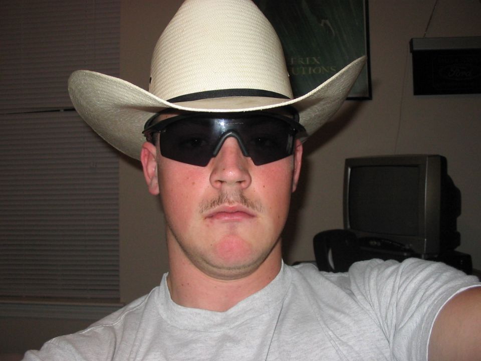 Man in cowboy hat and sunglasses, light gray t-shirt, with a small mustache
