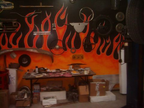 1978 Ford Bronco - A cluttered garage scene features a vibrant flame mural on the wall, adorned with various car parts and a license plate.