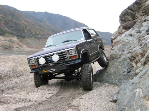 1985 Ford Bronco - This Ford Bronco is navigating a rocky, off-road terrain with a mountain landscape in the background.