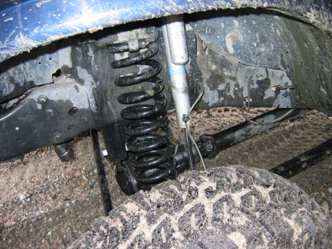 1985 Ford Bronco - Close-up view of the muddy suspension system and tire of a blue vehicle.
