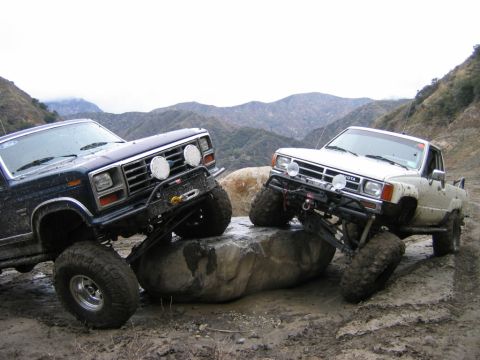 1985 Ford Bronco - Two modified trucks, a Ford and a Toyota, navigate a rocky trail in a mountainous landscape.