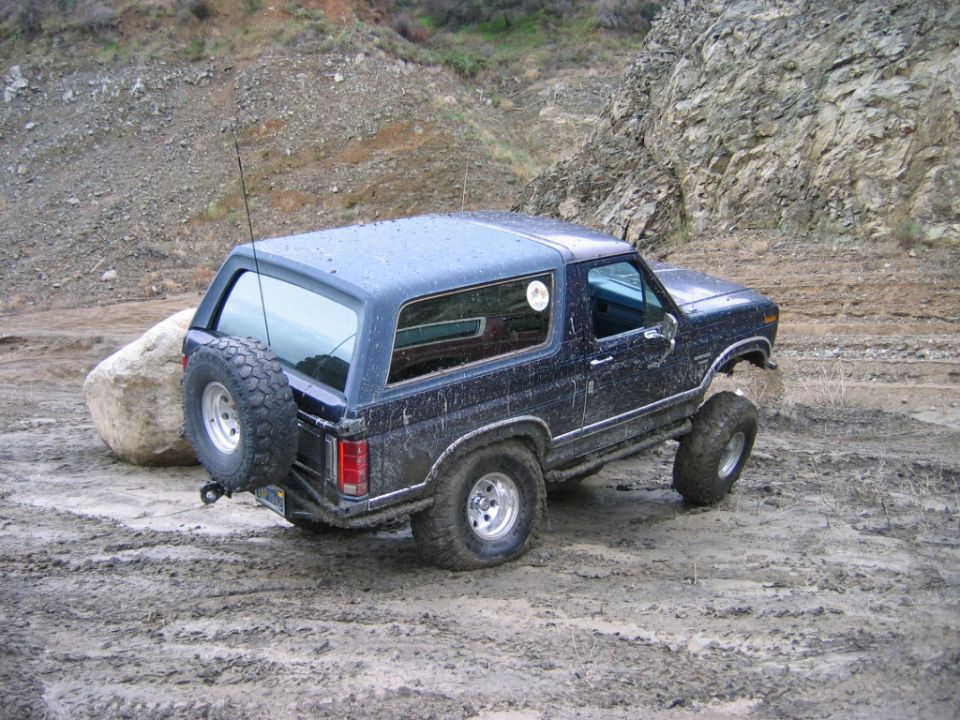 Dark blue lifted two-door Ford Bronco SUV on mud tires, rear 3/4 view in muddy quarry.