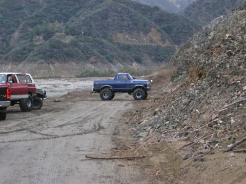 1985 Ford Bronco - Two off-road vehicles navigate a dusty, mountainous terrain.