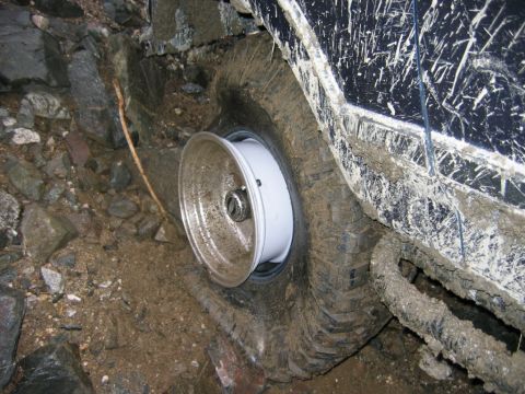 1985 Ford Bronco - Off-road vehicle with a flat tire stuck in rocky, muddy terrain.