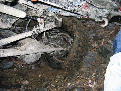1985 Ford Bronco - Mud-covered suspension and tire of an off-road vehicle navigating rocky ground.