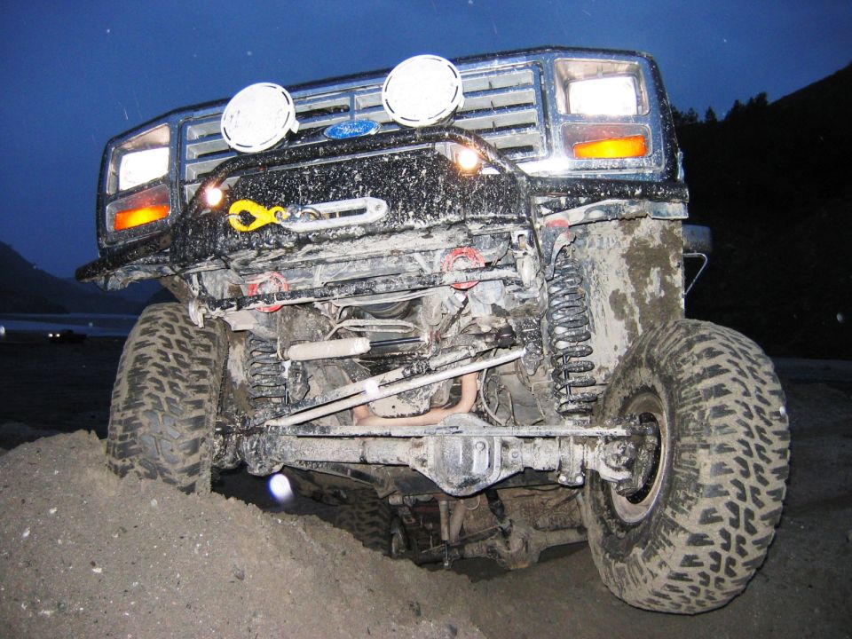 Muddy black Ford Bronco front, showing lifted solid axle, coils and big tires at dusk