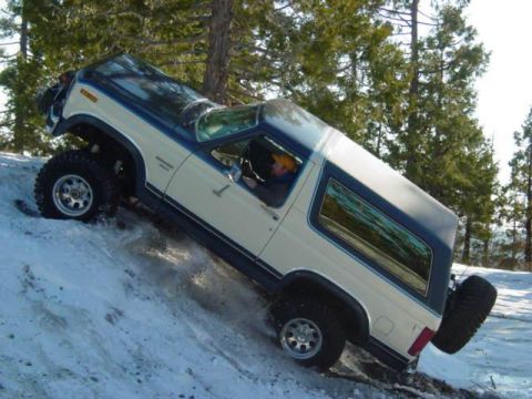 1986 Ford Bronco - A two-tone Ford Bronco navigates a steep, snow-covered hill.