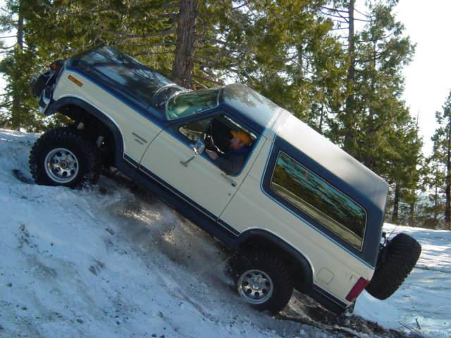 White and blue Ford Bronco with off-road tires driving on a snowy incline