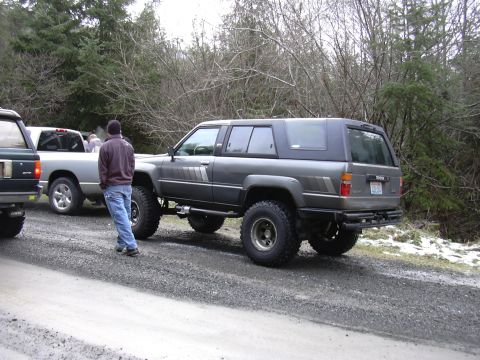 1991 Ford Bronco - A lifted SUV with a cap sits on a gravel road next to another vehicle.