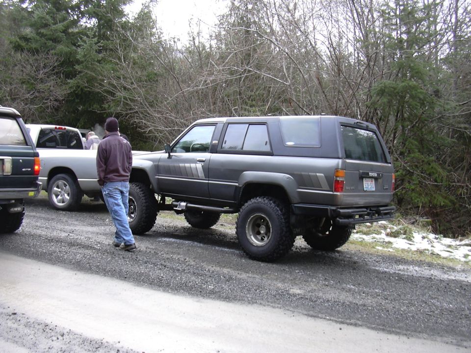 Dark gray SUV with a cap, lifted suspension, and off-road tires, viewed from the rear three-quarter angle