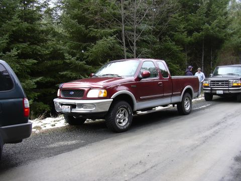 1991 Ford Bronco - Maroon 1997 Ford F-150 pickup truck is parked on a gravel road with trees in the background.