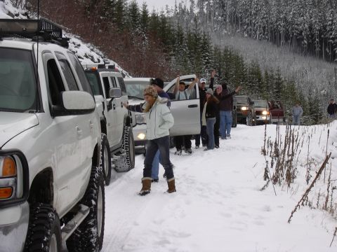 1991 Ford Bronco - A line of SUVs are parked in a snowy forest, with people standing next to them.