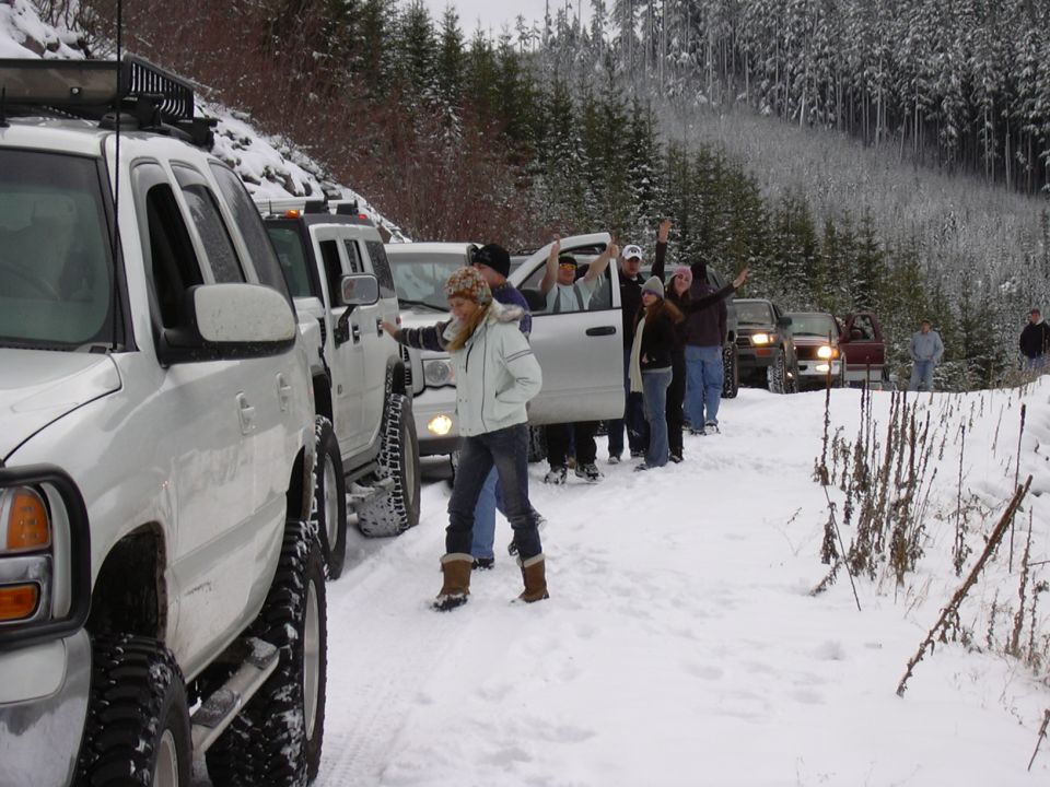 White SUV with roof rack in snowy forest, people standing by