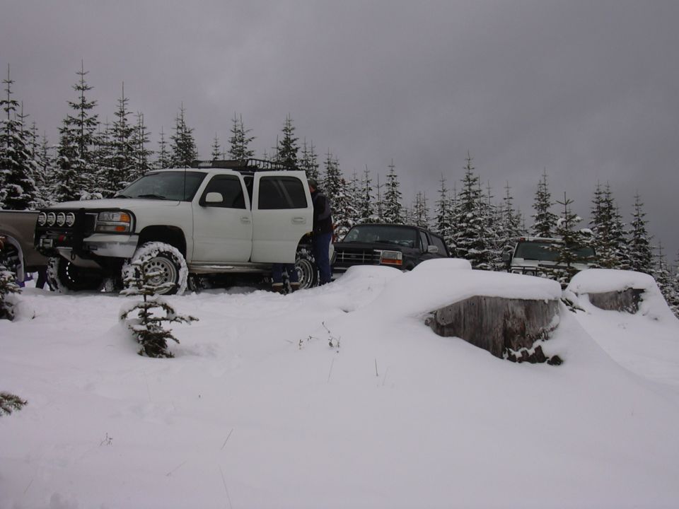 White SUV with roof rack and off-road lights in snow, parked next to other vehicles