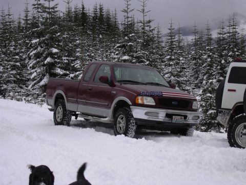 1991 Ford Bronco - A maroon Ford F-150 pickup truck with an American flag decal sits in the snow beside a white SUV.
