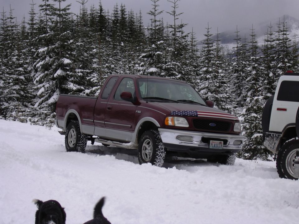 Maroon Ford F-150 pickup with American flag decal on hood parked in snow next to a white SUV