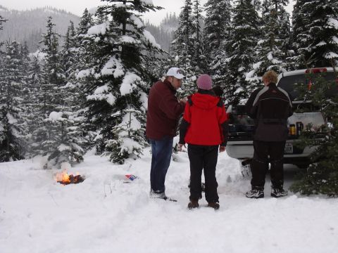 1991 Ford Bronco - People gather around a campfire in a snowy forest, with a pickup truck nearby.