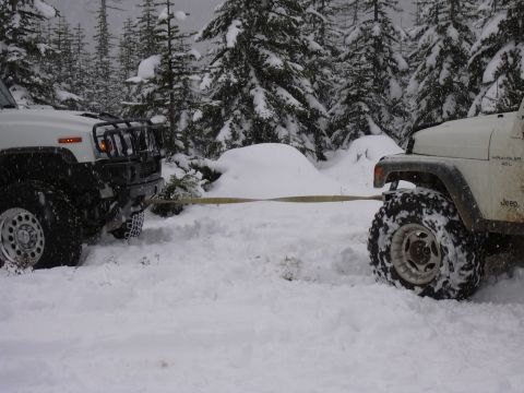 1991 Ford Bronco - Two off-road vehicles are stuck in the snow and one is being towed by the other.