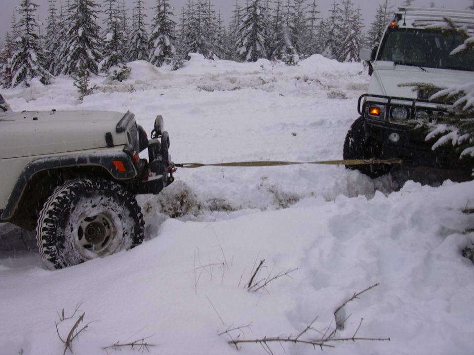Two off-road vehicles are stuck in deep snow, one towing the other
